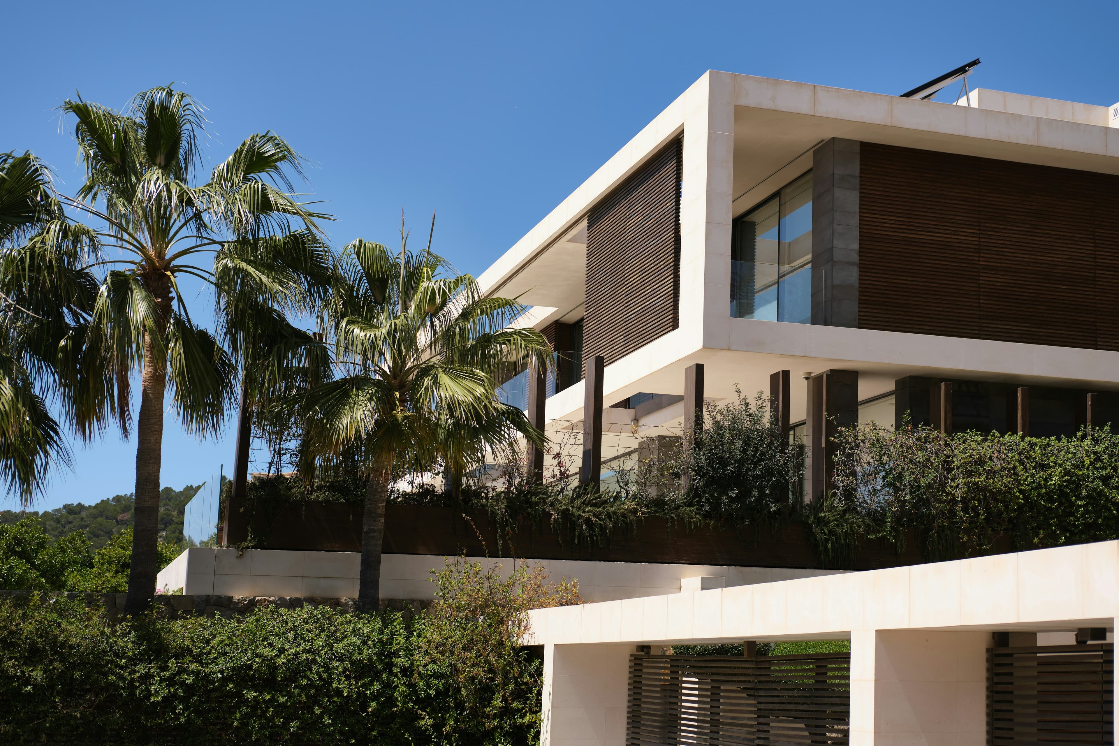 A white modernist villa with timber-screened terraces, framed by palm trees